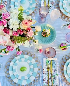 the table is set with plates, silverware and pink flowers on blue napkins