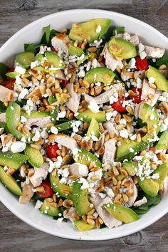 a salad with chicken, avocado and feta cheese in a white bowl