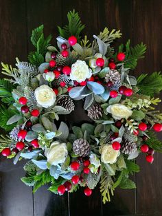 a wreath with red berries, white flowers and green leaves on a wooden table in front of a door