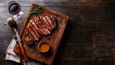 grilled steak served on wooden board with wine glasses and utensils, top view