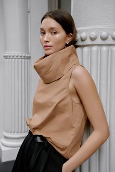 Make a statement with the Marcy Sleeveless Top, a structured and sleek shirt that transforms into a turtleneck. Marcy's unique turtleneck can be worn in two ways — fold in half to wear it gathered at the neckline, or amp up the oversize by standing up the collar for free-form volume. Crafted from 100% European poplin cotton, Marcy provides effortless day-to-night styling possibilities. [SPLIT] Yada, in chestnut, is 5'9" (175 cm) tall, wearing size XS. Sam, in light beige, is 5'8" (173 cm) tall, Chic Stretch Turtleneck Blouse, Modern High Neck Tops For Workwear, Chic Turtleneck Tops For Layering, Fall Workwear Cowl Neck Top, Chic Turtleneck Top, Sleeveless Blouse For Fall Layering, Brown High Neck Top For Work, Brown Turtleneck Top For Work, Sleeveless Blouse For Fall Workwear