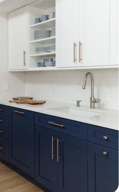 a kitchen with blue cabinets and white counter tops, gold pulls on the cupboards