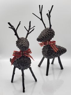 two metal reindeer statues with red bows on their heads and antlers in the shape of pine cones