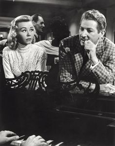 an old black and white photo of two people sitting at a piano with their hands on the keyboard