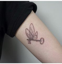 a small key tattoo on the arm with a dragonfly attached to it's side