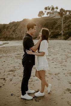 a man and woman standing on top of a sandy beach