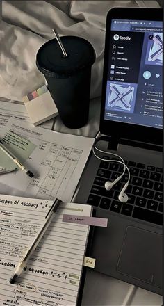 an open laptop computer sitting on top of a bed next to a cup and pen