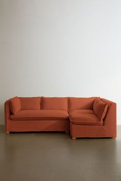 an orange sectional couch sitting on top of a wooden floor next to a white wall