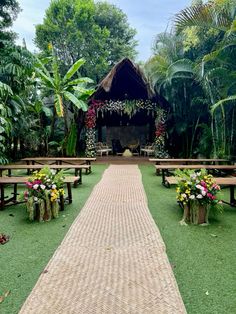 an outdoor ceremony setup with benches and flowers on the grass, surrounded by palm trees