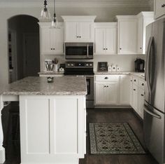 a kitchen with white cabinets and stainless steel appliances, including an island in the middle