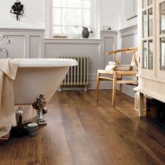 an old fashioned bathtub in a white bathroom with wood floors and walls, along with a wooden chair