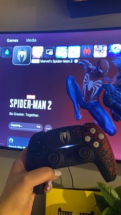 a person holding a video game controller in front of a tv with spider - man 2 on it