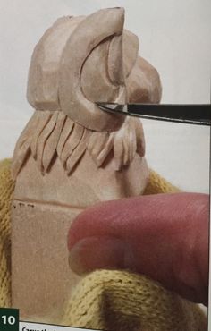 a hand holding a pair of scissors near a carved animal