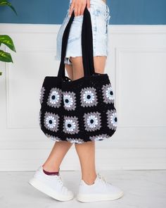 a woman carrying a black crocheted bag with blue and white flowers on it