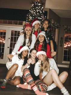 a group of young women sitting next to each other in front of a christmas tree