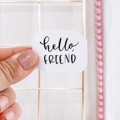 a person holding a sticker with the word hello friend on it in front of a white tile wall