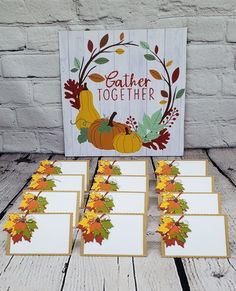 thanksgiving place cards with fall leaves and pumpkins on them, in front of a sign that says gather together