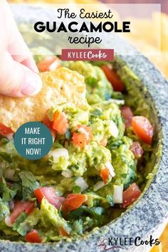 a hand dipping guacamole into a bowl with tortilla chips on the side