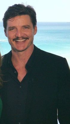 a man and woman standing next to each other in front of the ocean with a moustache on their face