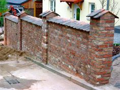 an old brick fence in front of a house with a red tiled roof and two chimneys