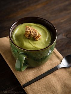 a green soup with croutons in it on a place mat next to a spoon