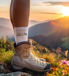 a person standing on top of a grass covered hillside wearing hiking boots and socks with the sun in the background