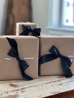 three wrapped presents sitting on top of a table next to each other with black ribbons