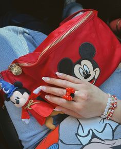 a woman's hand with mickey mouse on it holding a red purse and some other items