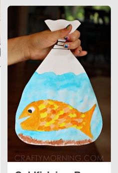 a hand holding up a paper bag with a fish on it and water in the bottom