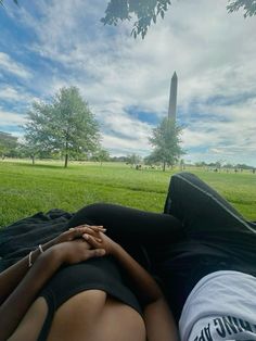 two people laying in the grass with their hands on each other's back, looking up at the washington monument