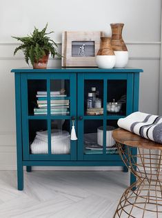 a blue cabinet with glass doors and shelves filled with towels, toiletries and vases