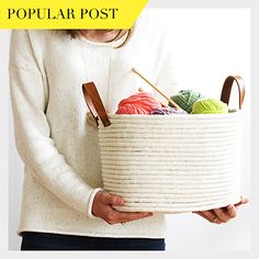 a woman is holding a basket with yarn and knitting needles in it while wearing a white sweater