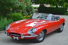 an old red sports car is parked on the side of the road in front of some bushes