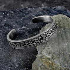 a silver bracelet sitting on top of a rock next to a piece of metal with an intricate design