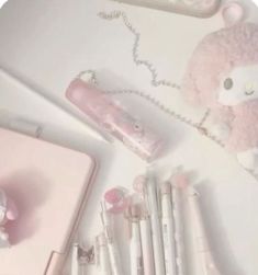 a pink teddy bear is sitting next to some pens and pencils on a white surface