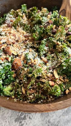 a wooden bowl filled with broccoli covered in nuts and parmesan cheese