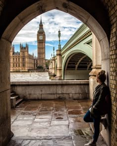 a woman standing in an archway looking out at the water and big ben clock tower