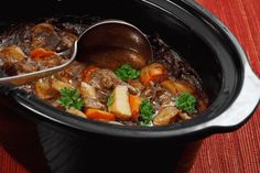 a crock pot filled with beef stew and carrots, garnished with parsley