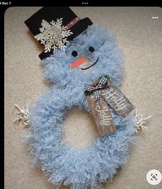 a blue snowman wreath on the floor with a hat and name tag attached to it