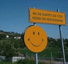 a yellow smiley face sign sitting on top of a metal pole next to a lush green field