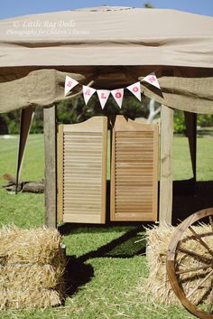 a wooden wagon sitting under a tent on top of a grass covered field next to hay bales