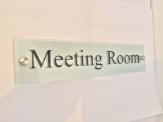 a glass sign that says meeting room on the side of a white wall next to a door