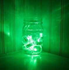 a mason jar filled with ice sitting on top of a wooden table next to a green light