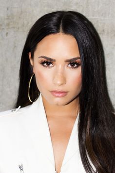 a woman with long black hair wearing large hoop earrings and a white blazer jacket