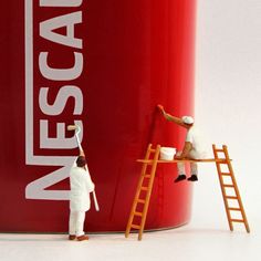 two figurines are painting the side of a large red can with escape logo on it