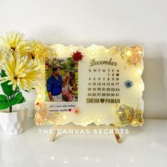 a personalized photo frame with lights and flowers on a table next to a potted plant