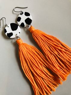 cow print earrings with orange tassels and black dots on the earring hooks