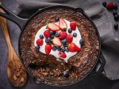 a chocolate cake with strawberries and blueberries on top is served in a cast iron skillet