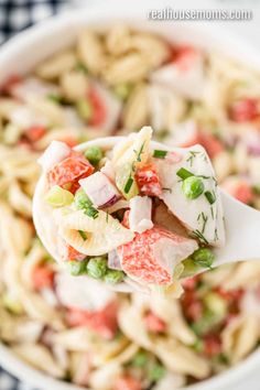 a spoon full of pasta salad being held by a person with a white bowl in the background