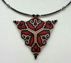 a red and black beaded triangle necklace on a white surface with beads hanging from it